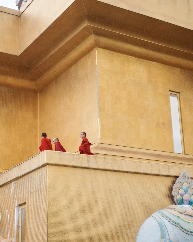 Three monks in maroon robes on a golden balcony