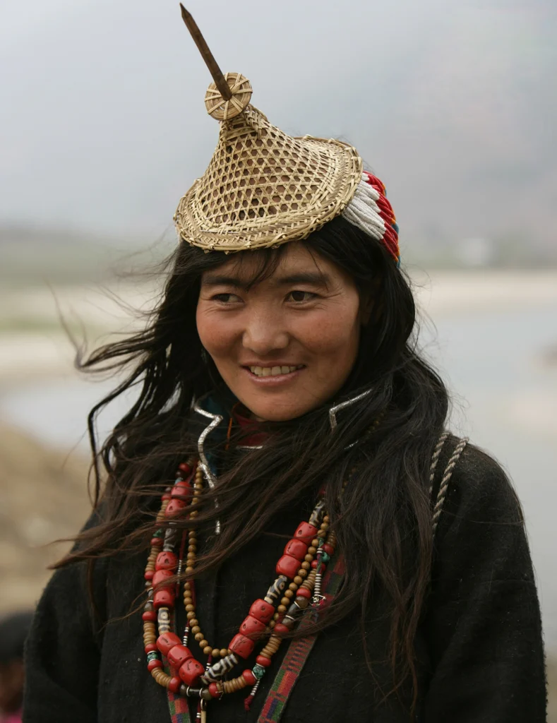 A smiling woman wearing a conical bamboo hat and a coral and turquoise necklace